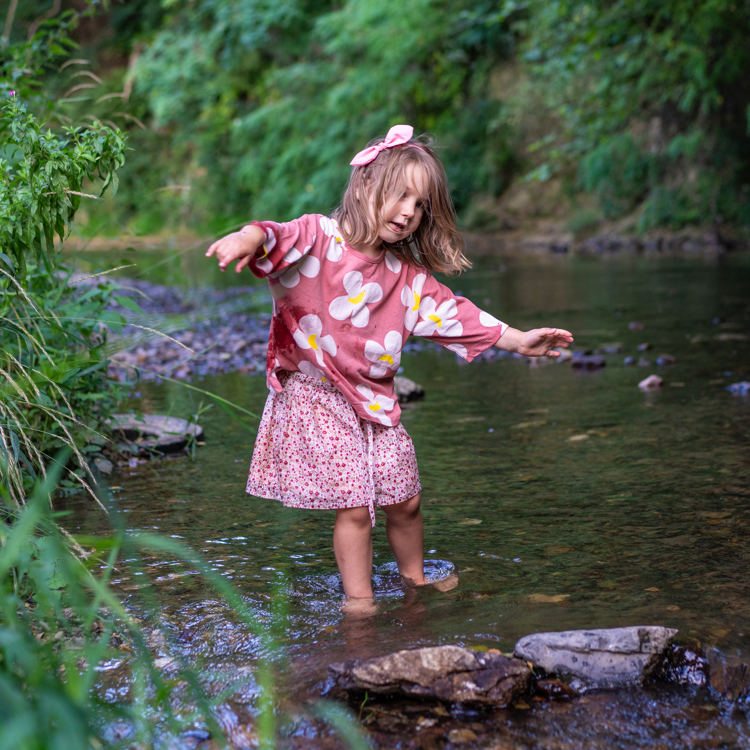 Meisje met roze rokje en truitje speelt op blote voeten in de rivier (Voer). 